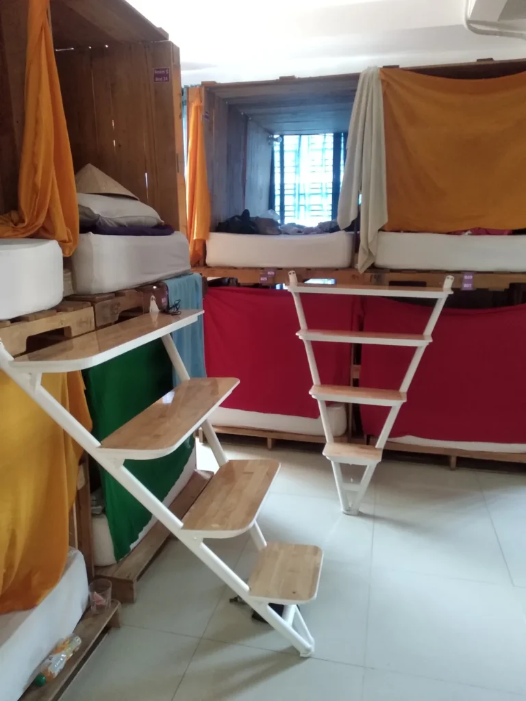 A dorm at DaBlend Hostel: wooden bunk beds with curtains and a white ladder (2019)